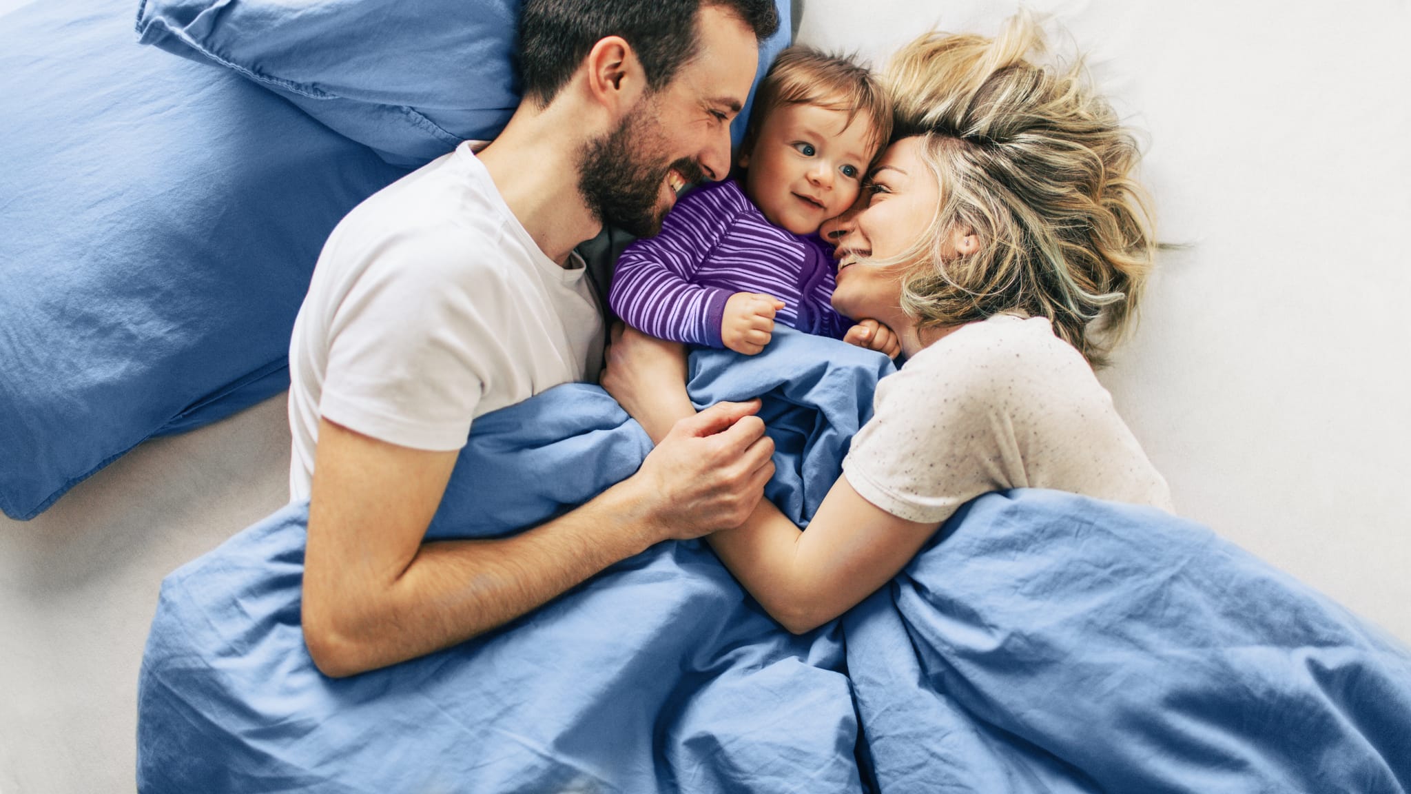 Family of three, a man, woman, and child, lying on a Sleepyhead bed with blue bedding.