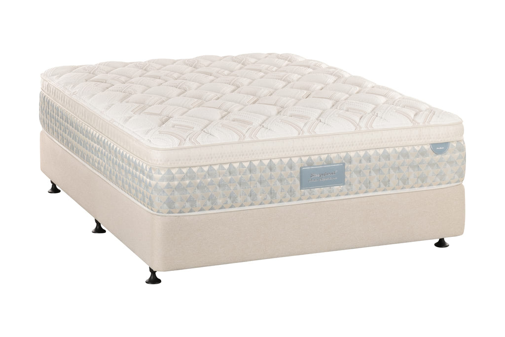 A Sleepyhead mattress on a matching upholstered bed base, photographed on a seamless white background. The mattress features a quilted cream top, a patterned side panel with blue and white geometric motifs, and a beige base with small black feet.