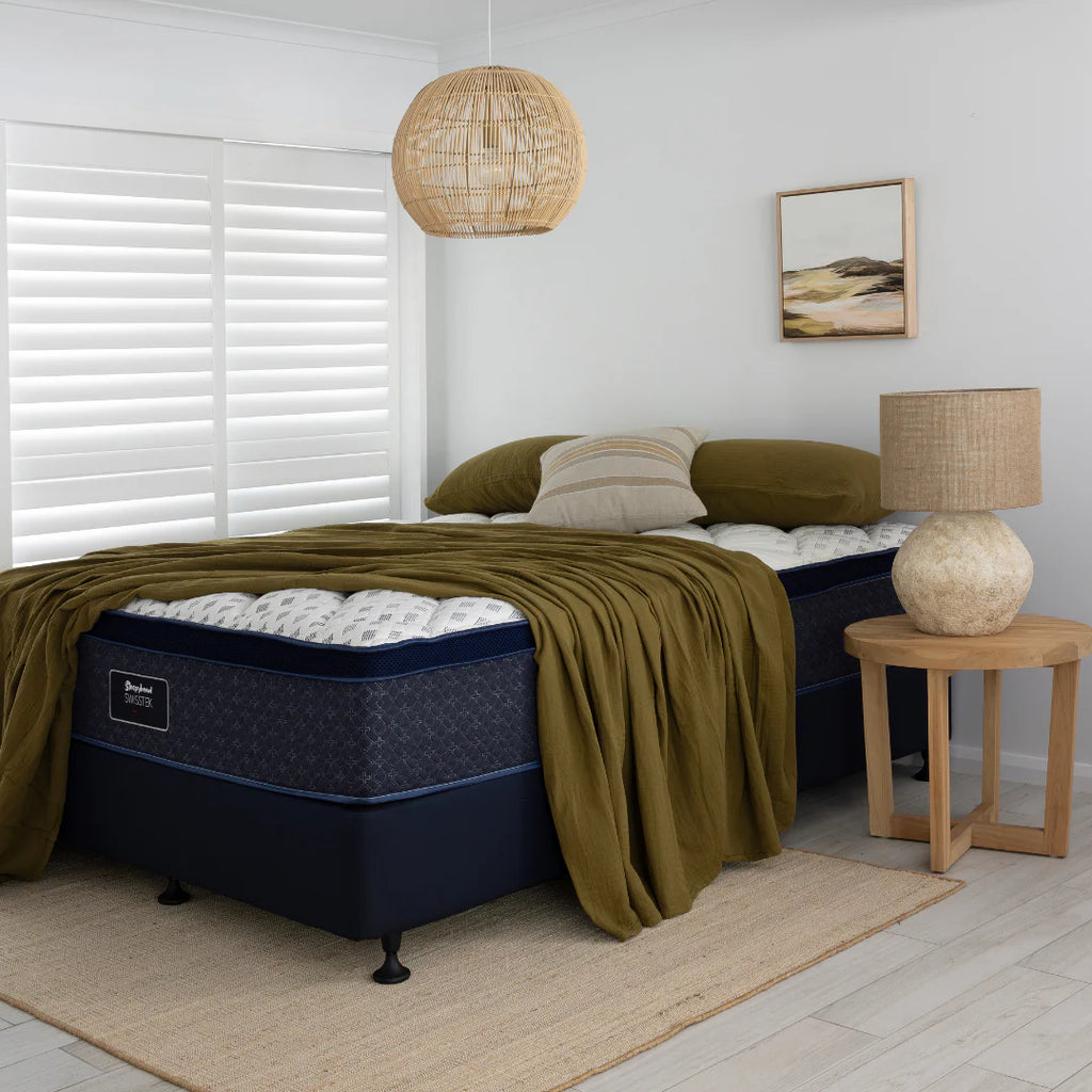 Sleepyhead bed with green blanket and pillows in a bedroom setting with a lamp and decor.