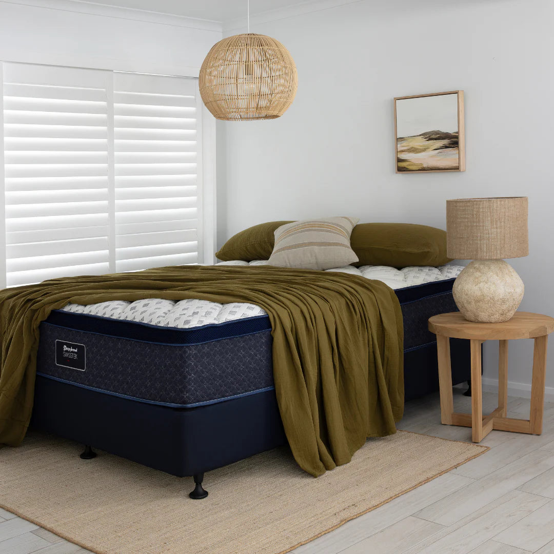 Sleepyhead bed with green blanket and pillows in a bedroom setting with a lamp and decor.