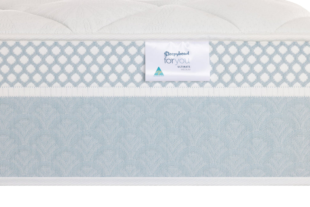 Close-up of a mattress side panel showing a white brand label that reads 'Sleepyhead For You Ultimate' against a light blue and white patterned mattress cover.