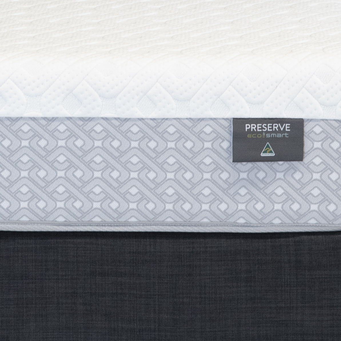 Close-up of a Sleepyhead mattress side panel showing the white quilted top, a light gray patterned middle band with a black Preserve label, and a dark charcoal fabric base.