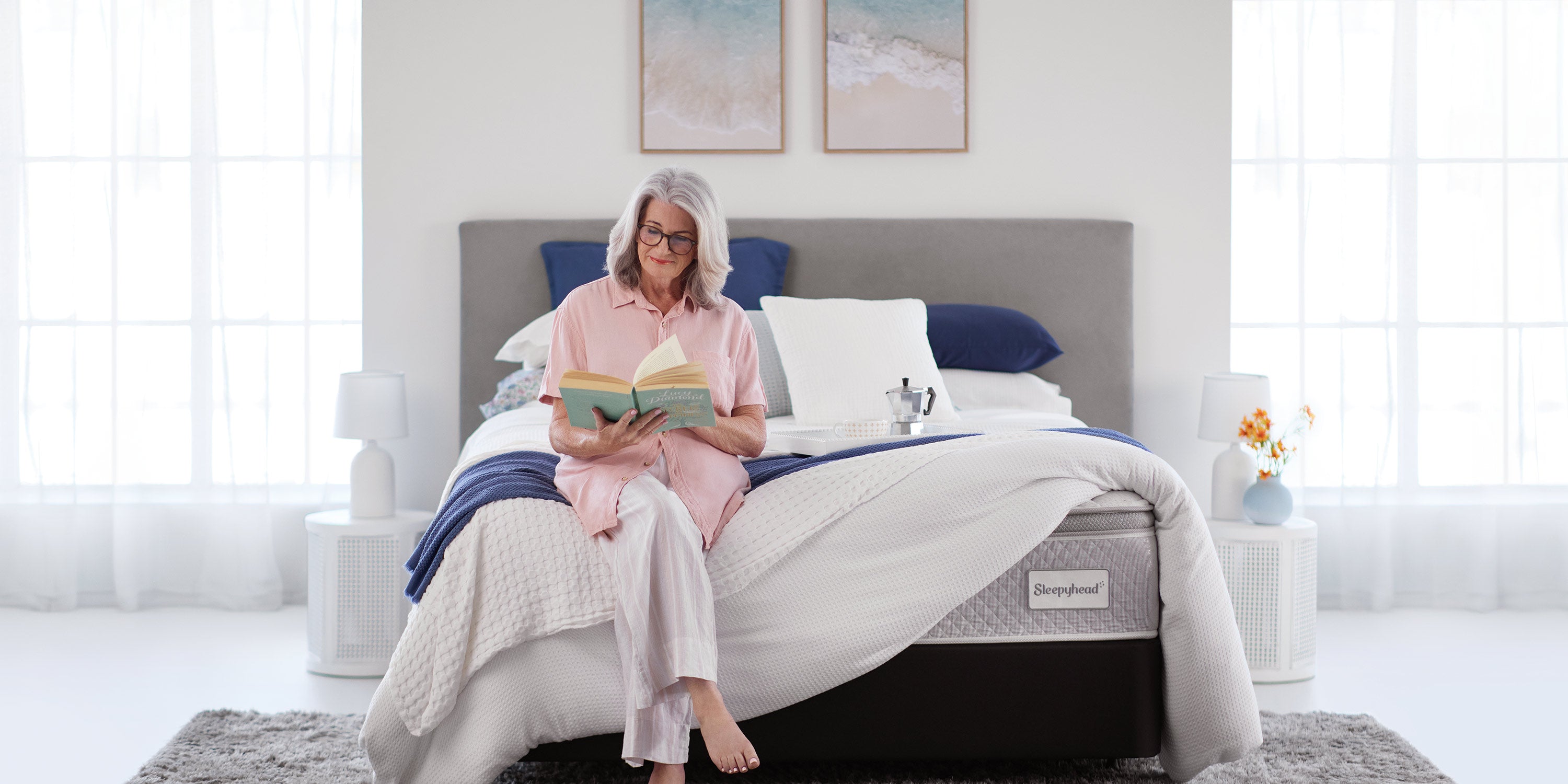 Woman sitting on a Sleepyhead bed reading a book in a bright bedroom