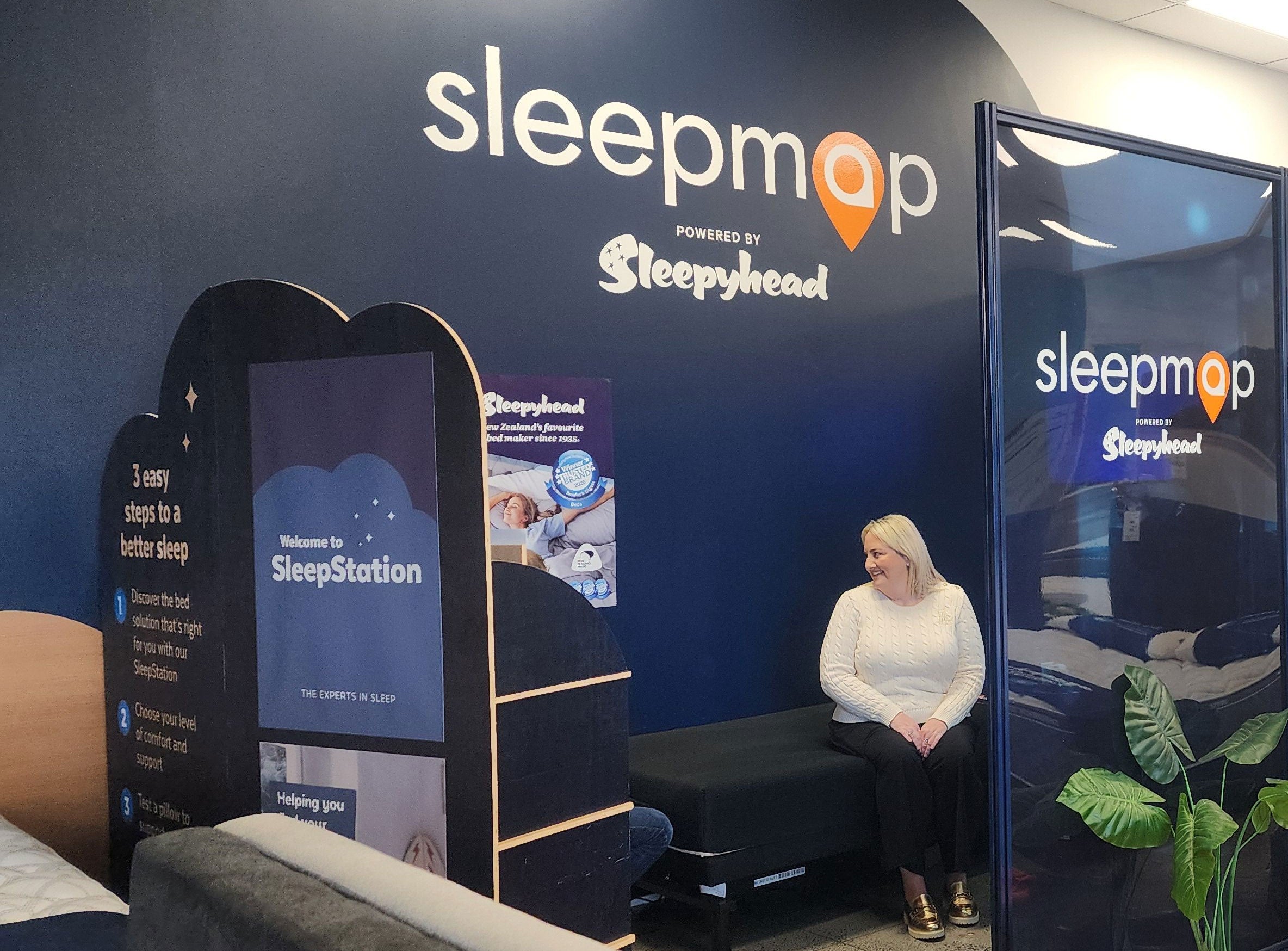 Person sitting on a bench in front of Sleepmap branded display with promotional materials.